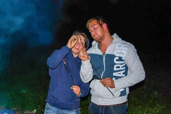 Zwei Personen halten Äste über einem kleinen Feuer