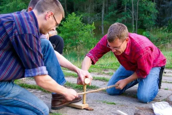Zwei Personen nutzen eine Holzbohrmaschine zur Herstellung von Feuer