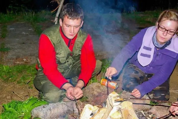 Zwei Personen sitzen am Lagerfeuer und rösten Essen auf Stockspießen