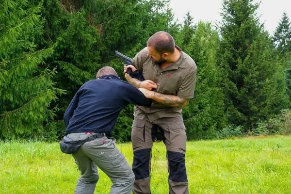 Zwei Personen üben eine Nahkampfsituation im Freien mit einer Waffe