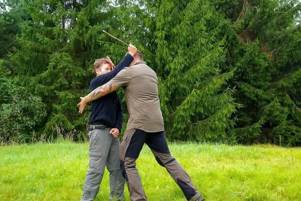 Zwei Personen üben eine Selbstverteidigungstechnik im Freien mit einem Stock