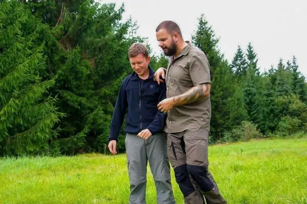 Zwei Personen unterstützen sich gegenseitig beim Gehen auf einer Wiese
