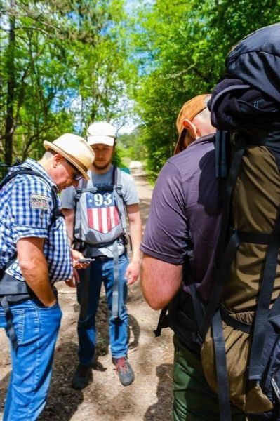 Drei Personen mit Rucksäcken stehen auf einem Waldweg und betrachten ein Smartphone