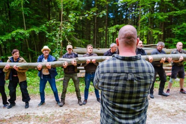 Gruppe hebt gemeinsam einen langen Baumstamm an einem Waldweg