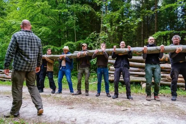 Gruppe hebt gemeinsam einen langen Baumstamm an einem Waldweg