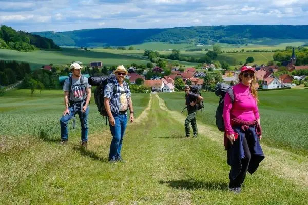 Gruppe mit Rucksäcken wandert auf einem Feldweg in ländlicher Umgebung