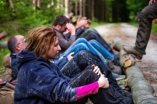 Gruppe sitzt auf Baumstämmen und bearbeitet Holzstücke im Wald