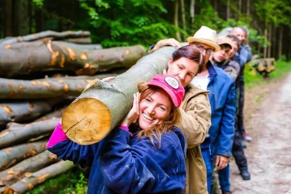 Gruppe trägt einen langen Baumstamm entlang eines Waldweges
