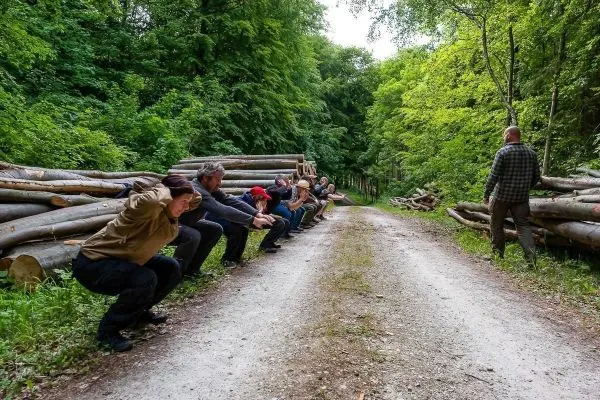 Gruppe von Personen in Hocke-Position entlang eines Waldweges, Holzstämme im Hintergrund