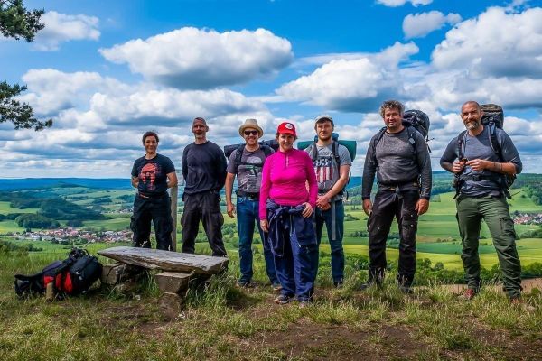 Gruppe von Wanderern steht vor einer Aussicht auf eine grüne Landschaft mit Wolken