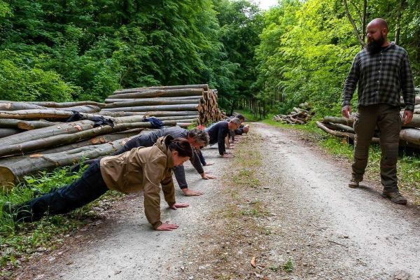 Gruppentraining mit mehreren Personen in Liegestützposition auf einem Waldweg