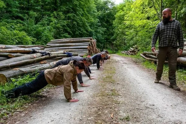Gruppentraining mit mehreren Personen in Liegestützposition auf einem Waldweg