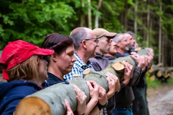 Gruppierung von Personen hält gemeinsam einen langen Baumstamm in der Natur
