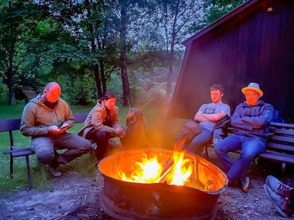 Kleines Bodenfeuer brennt in einem Metallring, umgeben von mehreren Personen