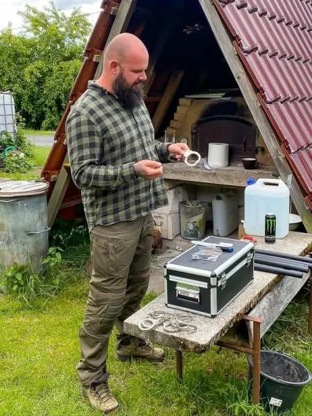 Mann hält zwei Ringe in der Hand, steht an einem Tisch mit Werkzeug und Ausrüstung