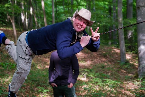 Mann überquert selbstgebaute Seilbrücke im Wald, hält sich mit beiden Händen fest