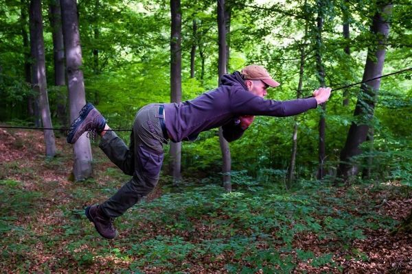Mann überquert selbstgebaute Seilbrücke zwischen Bäumen im Wald