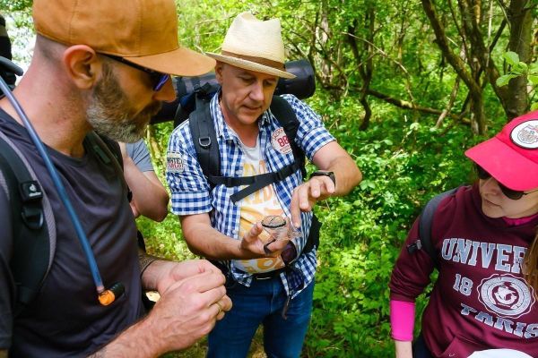 Mann zeigt Gruppe ein kleines Behältnis in der Natur