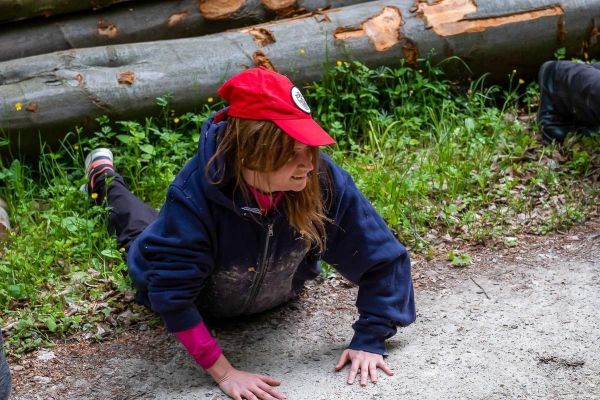 Person kriecht auf dem Boden entlang einer Waldstraße, umgeben von Baumstämmen