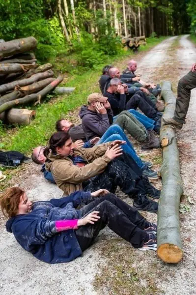 Teilnehmer führen eine Übung mit einem Holzstamm auf einem Waldweg durch