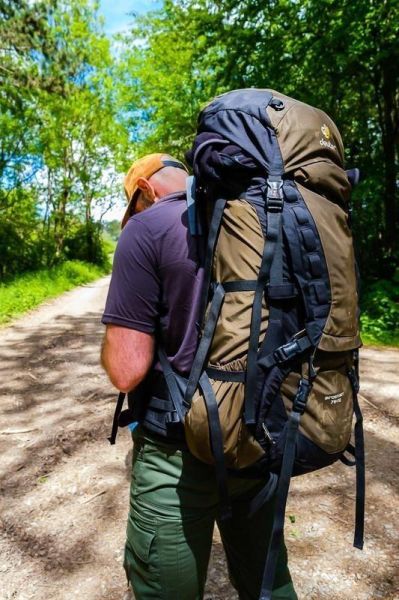 Wanderer mit großem Rucksack auf einem Waldweg, umgeben von Bäumen