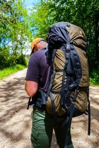 Wanderer mit großem Rucksack auf einem Waldweg, umgeben von Bäumen