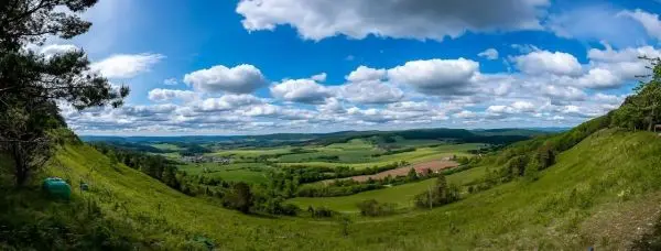 Weite Landschaft mit Hügeln, Wiesen und Wolken am Himmel