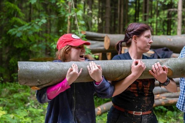 Zwei Personen tragen einen dicken Baumstamm durch den Wald