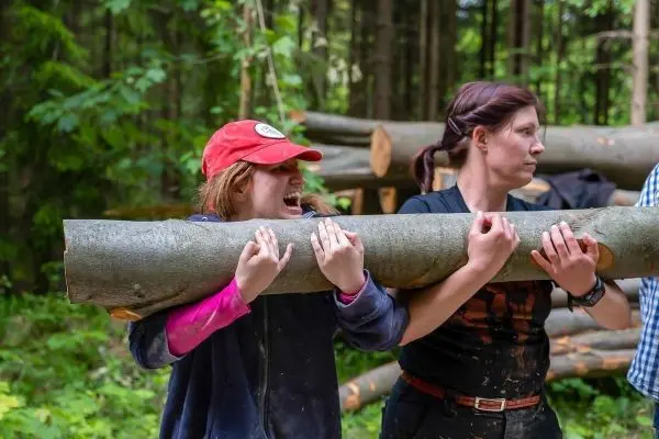 Zwei Personen tragen einen dicken Baumstamm durch den Wald