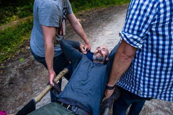 Zwei Personen tragen einen Mann auf einer improvisierten Trage aus Holz