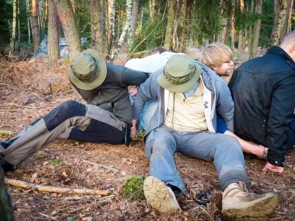 Drei Personen sitzen im Wald mit gefesselten Händen auf dem Boden