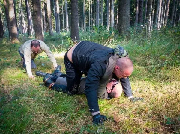 Drei Personen üben eine Bodenkampftechnik im Wald auf weichem Untergrund
