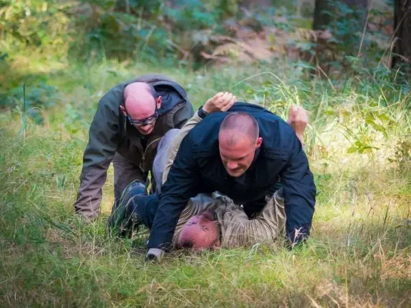 Drei Personen üben eine Kontrolle im Gras unter Bäumen aus