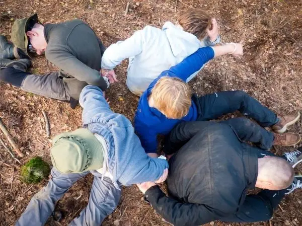 Fünf Personen sitzen im Kreis auf dem Boden und halten sich an den Händen