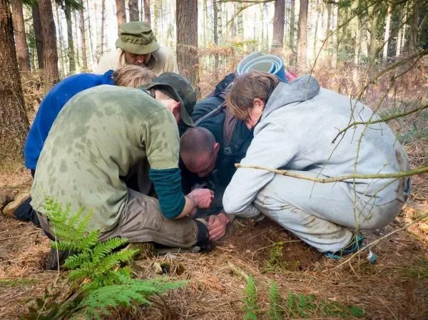 Gruppe beugt sich über den Boden im Wald, um etwas zu untersuchen