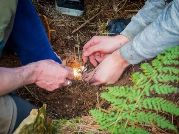 Hände zünden kleine Äste im Boden an beim Survival Training
