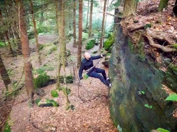 Kletterer nutzt einen Ast zur Unterstützung an einer Felswand im Wald