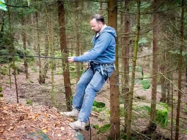 Mann in Kletterausrüstung führt Seilquerung zwischen Bäumen durch