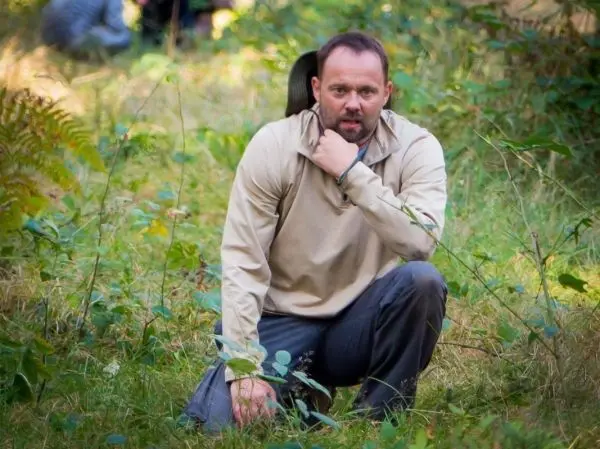 Mann kniet im Gras und betrachtet die Umgebung aufmerksam