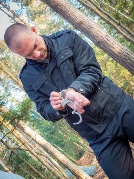 Mann mit Handschellen an den Handgelenken in einem Waldgebiet