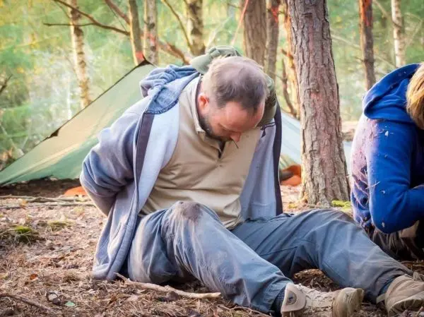 Mann sitzt am Boden mit gefesselten Händen in einem Waldgebiet