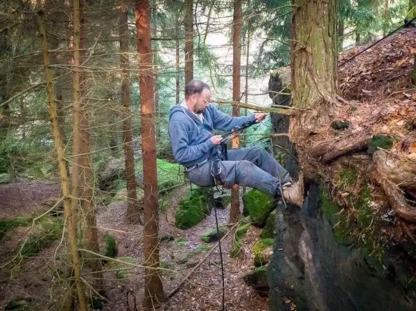 Mann sitzt an einem Felsen und sichert sich mit einem Seil im Wald