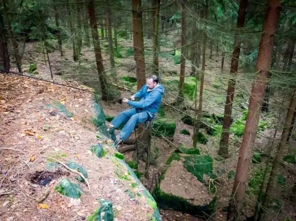 Mann überquert eine selbstgebaute Seilbrücke zwischen Bäumen im Wald