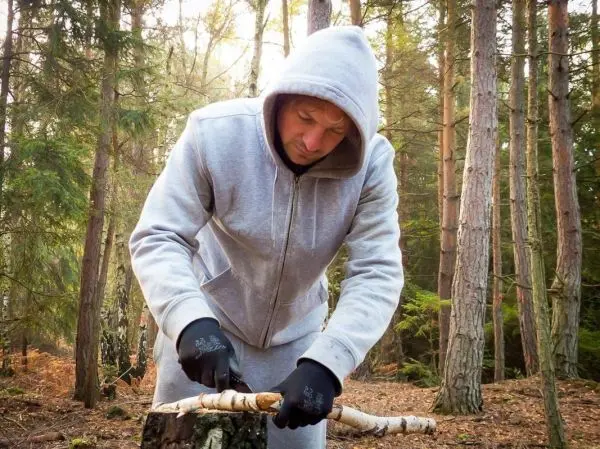 Messer schneidet Rinde von einem Holzstück im Wald
