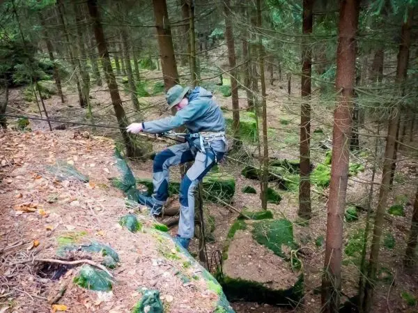 Person balanciert auf einer selbstgebauten Seilbrücke zwischen Bäumen