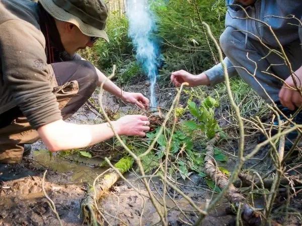 Person entzündet Feuer mit Zweigen im Wald beim Survival Training