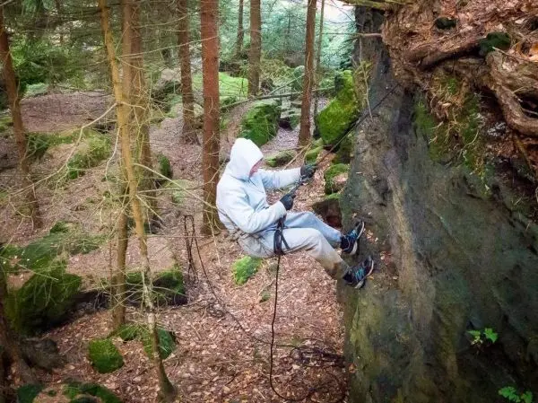 Person klettert mit Seil an einer Felswand im Wald