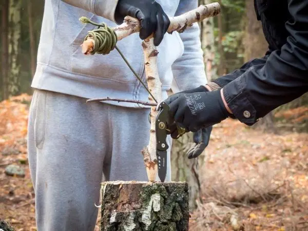 Person schneidet einen Stock mit einem Messer auf einem Baumstumpf