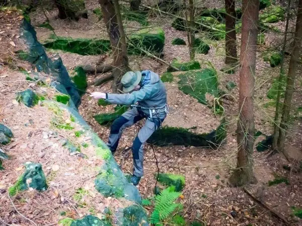 Person sichert sich beim Abseilen an einer steilen Felswand im Wald