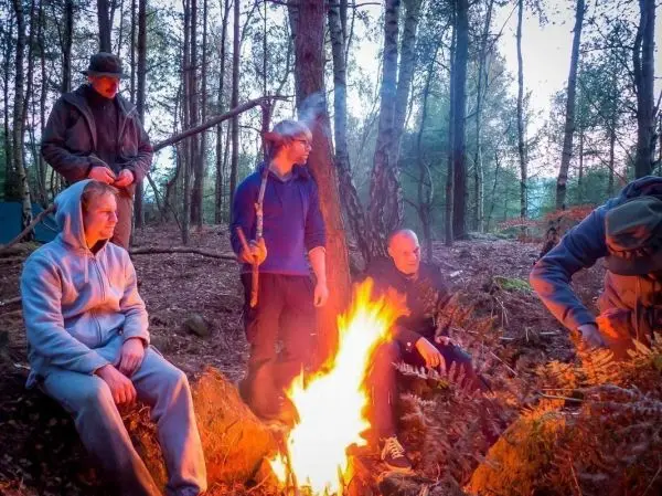 Personen sitzen um ein Feuer im Wald beim Überlebenstraining